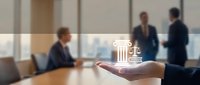 Corporate legal services concept with justice scales icon floating above open palm while business professionals meet in modern office boardroom.