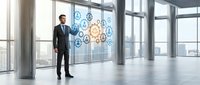 Professional businessman in dark suit standing in modern office space with large windows overlooking city, digital gear icons floating nearby representing innovation.