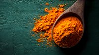Vibrant orange turmeric powder spilling from wooden spoon on dark green textured background, dramatic lighting creates contrast for culinary and wellness concept.