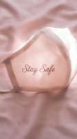 Pink fabric face mask with Stay Safe embroidery resting on soft rose textile, symbolizing health awareness and protection during pandemic.