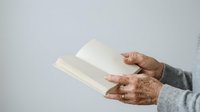 Senior adult with brown skin tone holding open blank white book or magazine against neutral background, suitable for publishing, education, and reading concepts.