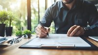 Professional signing business contract at wooden desk with green plants and natural light, focused on document details and pen in hand. Perfect for business concepts.
