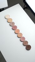 Makeup eyeshadow palette refills in nude brown tones arranged in curved line on white surface for cosmetic branding and beauty product photography.