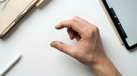 Caucasian male hand gesturing grab or pinch motion on white desk surface with notebook and pen, suitable for business, technology, and office design projects.