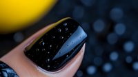 Glossy black manicure with water drops on nail surface against dark background with bokeh effect creates luxurious and mysterious atmosphere.