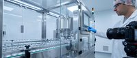 Pharmaceutical technician operating automated production line in sterile cleanroom facility. Quality control specialist monitoring manufacturing process.