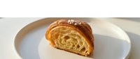 Freshly baked croissant with golden, flaky layers on white plate, ideal for bakery, food photography, and culinary design projects.