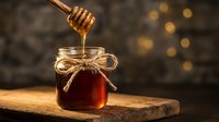 Golden honey dripping from wooden dipper into glass jar with twine bow on rustic wood board against warm bokeh background for natural organic food concepts.