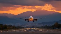 Commercial airplane approaching runway during dramatic sunset with mountain backdrop and runway lights for aviation travel concepts.