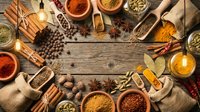 Aromatic spices and herbs arranged in wooden bowls on rustic table with cinnamon sticks, star anise, cardamom pods creating culinary frame for cooking.