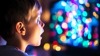 Young Caucasian boy gazing at colorful bokeh lights with wonder and amazement, side profile view showing genuine childhood excitement and holiday magic atmosphere.