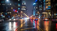 Blurred city street at night with wet asphalt reflecting colorful lights from buildings and traffic. Urban nightlife scene with bokeh effect and glowing windows.