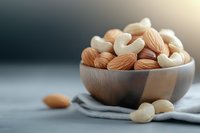 Mixed nuts almonds and cashews in wooden bowl on gray cloth with warm sunlight for healthy snacking and cooking ingredients.