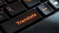 Illuminated orange translate button on black computer keyboard in dark environment, close-up macro shot showing technology and communication concept.
