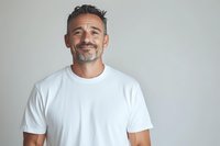 Mature Hispanic man with salt and pepper hair wearing white t-shirt smiling confidently against light gray background. Professional headshot for business or lifestyle content.