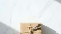 Kraft paper gift box tied with twine and decorated with dried botanical elements, isolated on white marble background for holiday packaging and design projects.