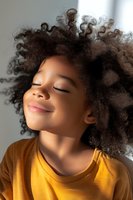 Young African American girl with natural curly hair and peaceful expression wearing yellow t-shirt, eyes closed in serene moment captured in soft natural light.