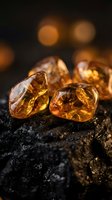 Raw amber gemstones with golden honey color and natural inclusions on dark textured surface with warm bokeh lighting for luxury jewelry design.