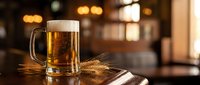Fresh golden beer mug with foam head on wooden bar counter in warm pub atmosphere with bokeh lights for hospitality and beverage marketing materials.