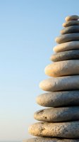 Balanced stack of smooth river stones creating zen tower against soft blue sky background for meditation and mindfulness concepts.