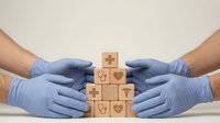 Healthcare professionals in blue medical gloves protecting wooden blocks with heart symbols representing patient care and medical protection services.
