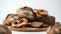 Assorted artisan breads including sourdough loaves, pretzels, and whole grain slices arranged on wooden board for bakery, food, and culinary design projects.