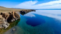 Dramatic coastal cliffs meet crystal clear turquoise waters along rocky shoreline, with deep blue ocean and peaceful sky creating serene natural seascape.