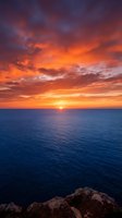 Dramatic ocean sunset with vibrant orange and golden sky meeting calm blue sea, rocky coastline in foreground. Perfect for travel, nature, and inspirational design projects.