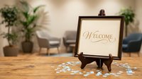 Elegant welcome sign on wooden easel with scattered flower petals in modern office lobby or reception area for hospitality and business greeting.