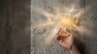 Hand reaching toward glowing trophy cup against textured concrete wall, symbolizing success, achievement, and winning goals for business and motivation concepts.