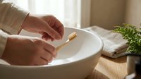 Eco-friendly bamboo toothbrush in hands over white ceramic sink. Sustainable dental hygiene routine in modern bathroom with natural lighting and plants.