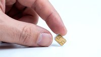 Close-up of hand holding small gold SIM card chip isolated on white background for technology and telecommunications concepts.