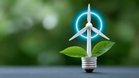 Miniature wind turbine with glowing blue light on light bulb base with green leaves, symbolizing renewable energy solutions against blurred natural background.