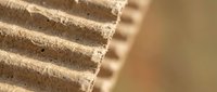 Corrugated cardboard sheets stacked showing textured brown paper layers and fluted structure for packaging and shipping materials.