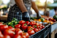 Fresh ripe red tomatoes in black crate at farmers market with person shopping for organic produce. Healthy eating and local agriculture concept.