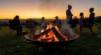 Group of friends gathering around campfire at sunset enjoying outdoor adventure and bonding time together in nature during golden hour camping trip.