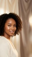 Young African American woman with curly hair smiling warmly in soft natural light wearing white sweater for lifestyle and wellness content.