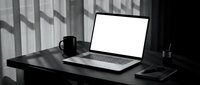 Modern minimalist workspace with open laptop displaying blank white screen on dark wooden desk with coffee mug and office supplies in monochrome setting.
