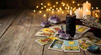 Tarot cards spread on wooden table with burning candles, amethyst crystals and warm bokeh lights creating mystical fortune telling atmosphere.