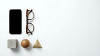 Modern workspace flat lay with smartphone, eyeglasses and geometric wooden shapes on clean white background for business and design projects.