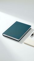 Closed teal hardcover notebook with blank pages positioned next to an open notepad and pen on a clean white surface with soft shadows.