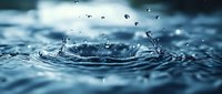 Water drops creating circular ripples on blue water surface with dramatic splash effect and floating droplets against moody cloudy sky background in macro photography.