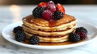 Stack of golden pancakes topped with fresh mixed berries including blackberries, raspberries and strawberries, drizzled with maple syrup on white plate, breakfast setting.