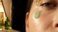 Young woman applying jade gua sha facial massage tool for skincare routine and natural beauty treatment in warm golden light.