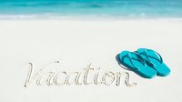Vacation written in sandy tropical beach with turquoise flip flops beside it, ocean waves in background, summer holiday travel concept.