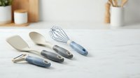 Set of modern kitchen utensils with blue handles on white marble countertop in contemporary home interior for cooking and food preparation.