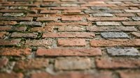 Weathered brick pavement with moss growing between aged red and brown stones creating rustic textured surface for architectural backgrounds.