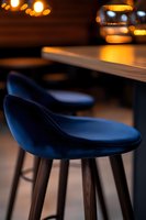 Modern navy blue velvet bar stools with wooden legs against blurred warm restaurant lighting create luxurious contemporary dining atmosphere.
