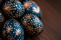 Navy blue Christmas ornaments with golden starburst pattern on dark wooden background create festive holiday mood. Selective focus adds depth to decorative spheres.