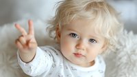Adorable blonde toddler with bright blue eyes showing peace sign while lying on white fur. Soft natural lighting creates gentle mood for family, childhood, and lifestyle designs.